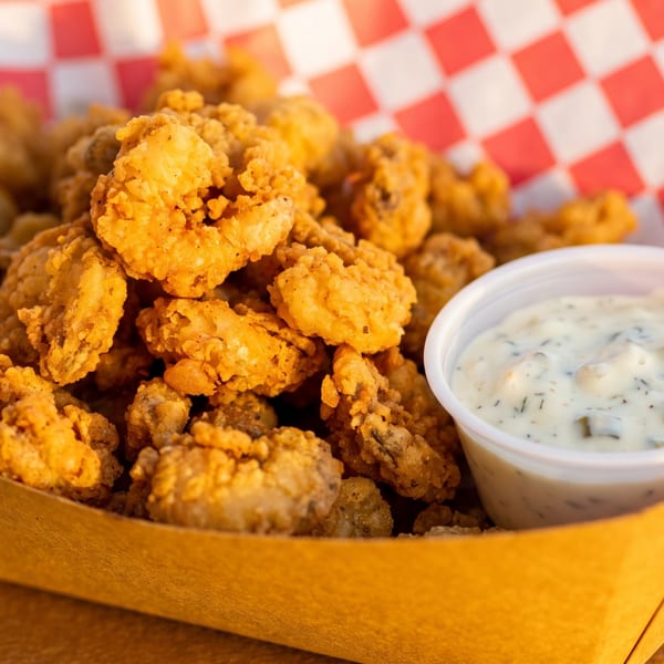 Golden fried popcorn shrimp in a paper tray with a side of tartar sauce.