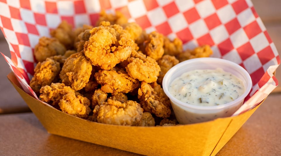 Golden fried popcorn shrimp in a paper tray with a side of tartar sauce.
