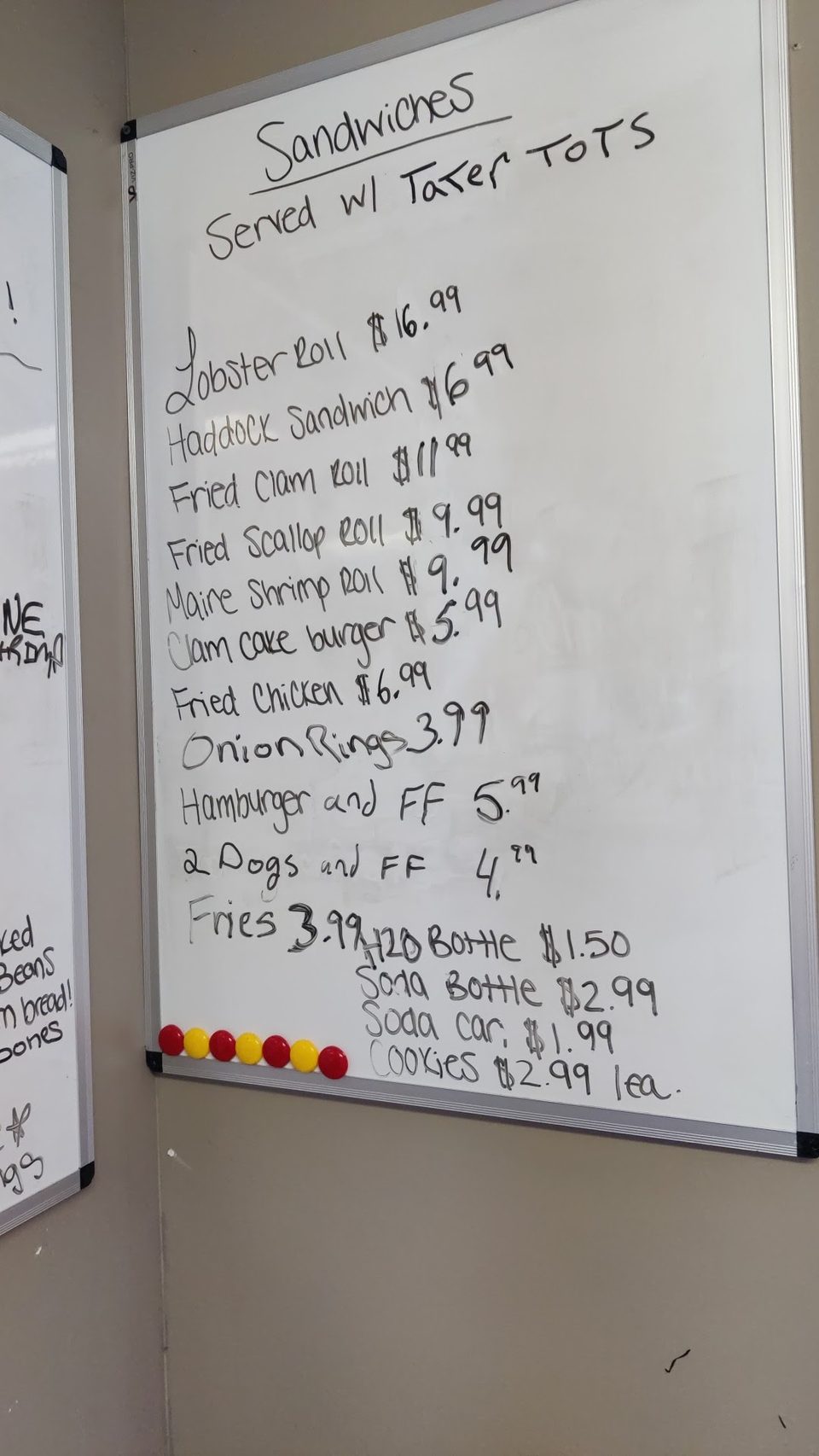 A handwritten menu on a whiteboard lists sandwiches, sides, and drinks with prices.