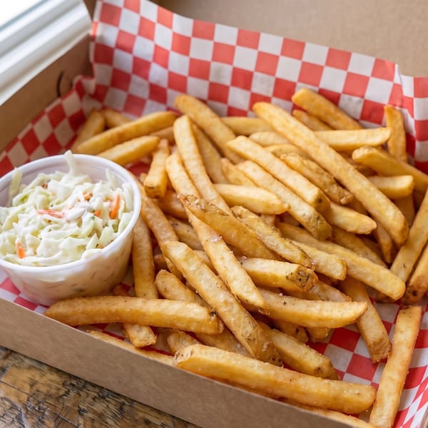 A cardboard takeout box filled with golden french fries and a side of coleslaw.