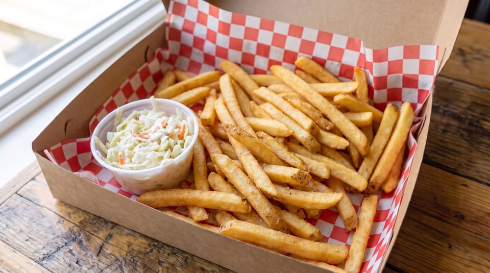 A cardboard takeout box filled with golden french fries and a side of coleslaw.