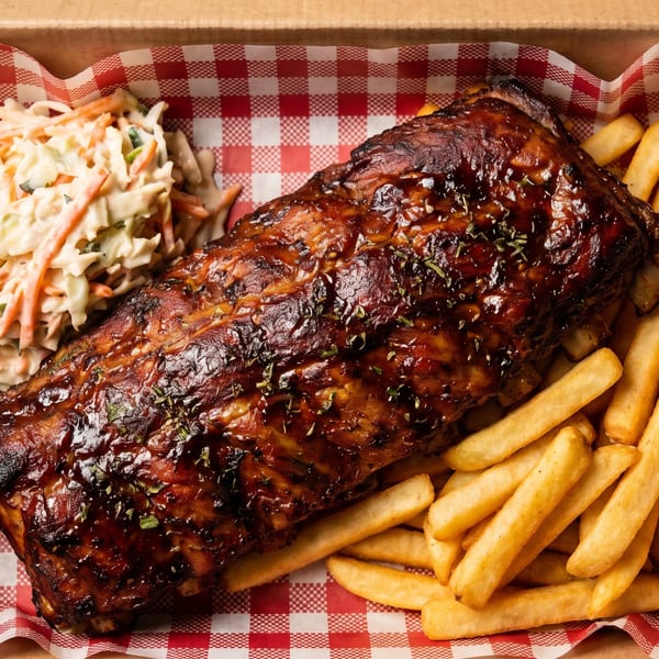 BBQ ribs with coleslaw and french fries in a takeout box with red and white checkered paper.